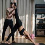 A yoga instructor helps a woman with flexibility exercises in a serene studio setting.
