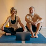 An elderly couple practicing yoga at home with online guidance, smiling and relaxed.